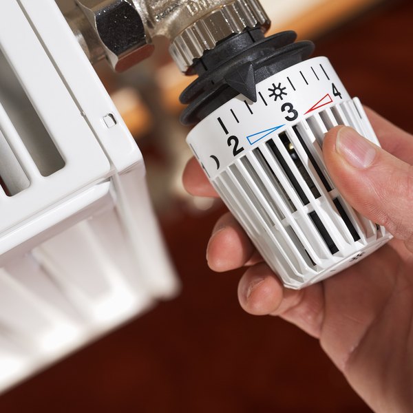 Hand stellt ein Heizkörper-Thermostat ein