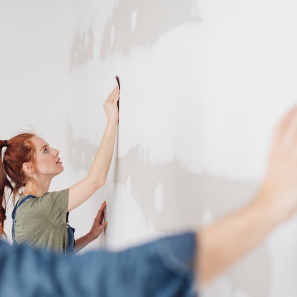 Paar spachtelt oder schleift eine Wand bei der Renovierung.